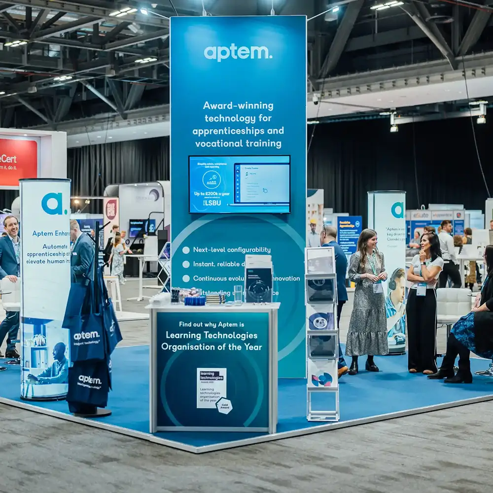 Aptem booth at a trade show with a tall blue display about apprenticeship technology and an award announcement.