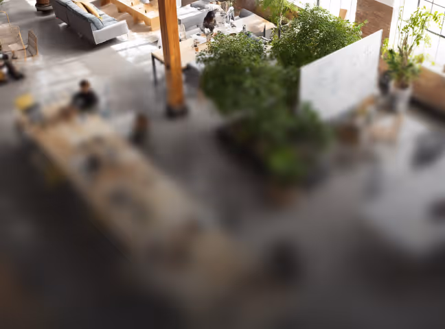 Moderne Büroräume mit natürlichem Licht, Sitzbereich, Pflanzen und Menschen bei der Arbeit.