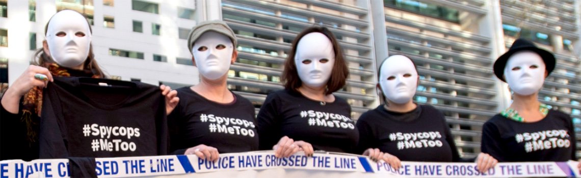 Protesters in white masks wearing '#Spycops #MeToo' t-shirts hold tape reading 'Police have crossed the line'