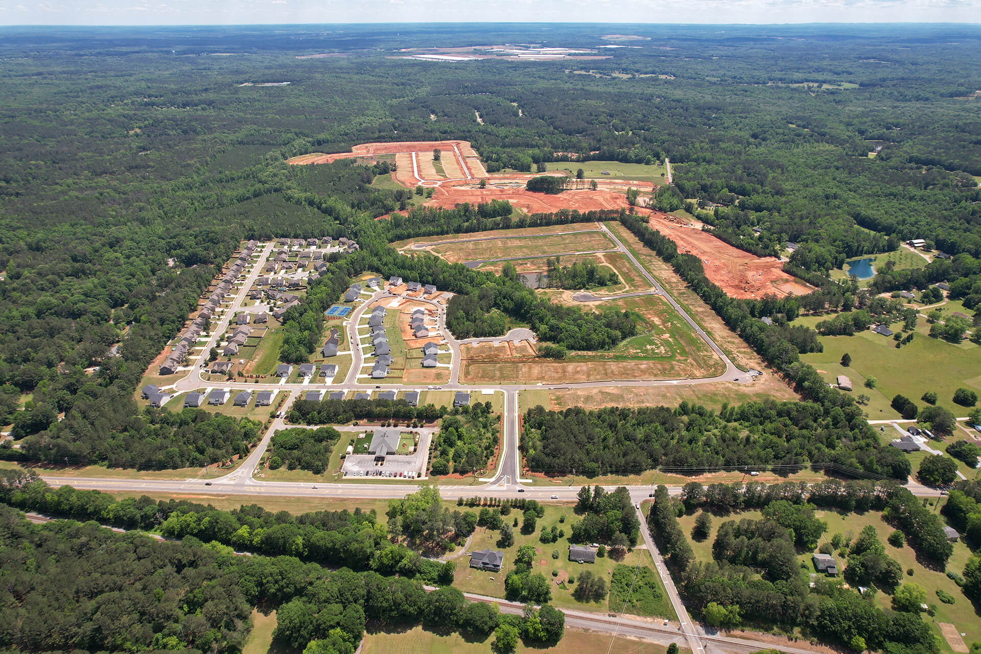 Aerial view of a suburban neighborhood with houses, roads, and a large area under construction surrounded by greenery.