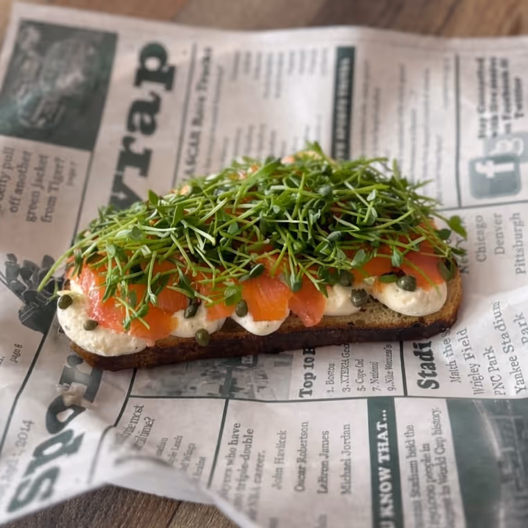 Open-faced smoked salmon sandwich with cream cheese, capers, and fresh greens on rustic bread.
