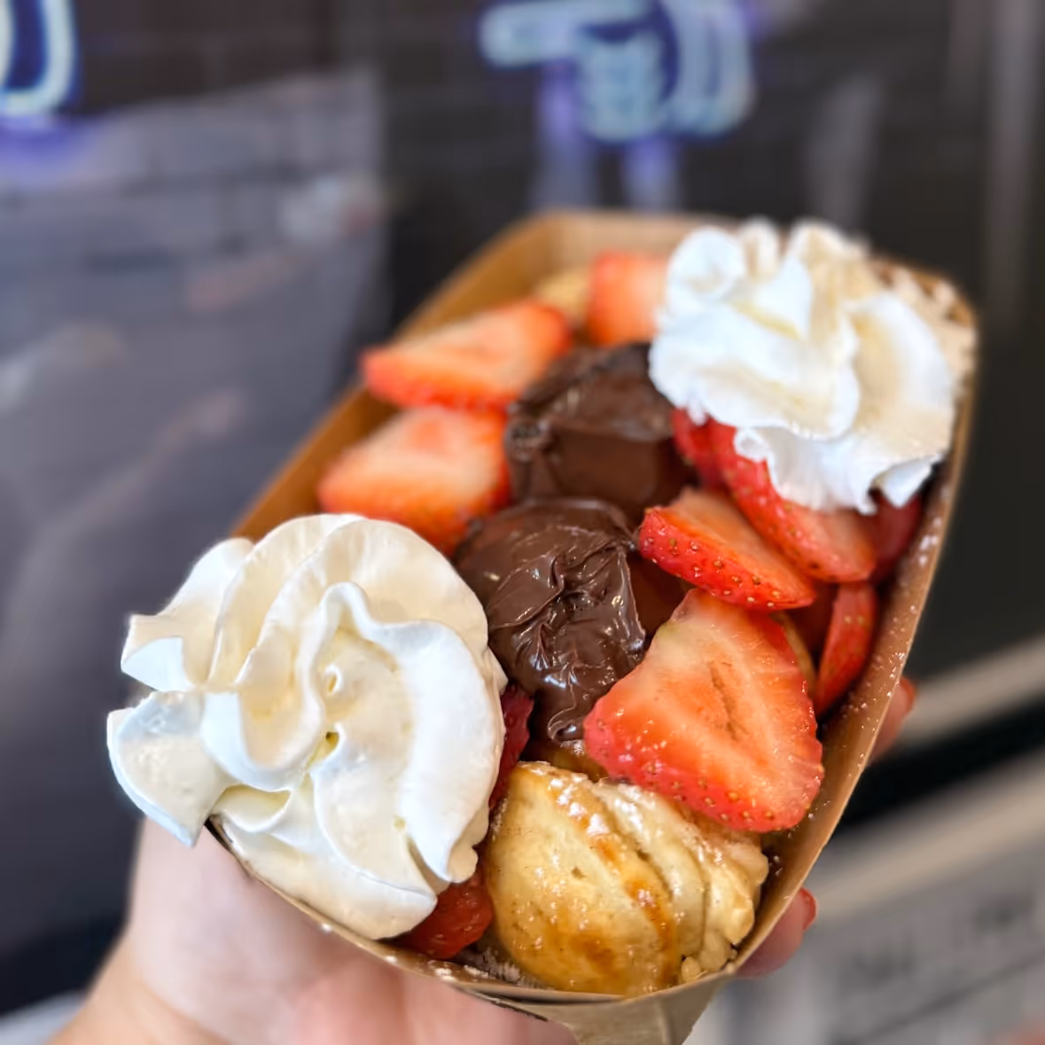 Hand holding dessert boat with strawberries, whipped cream, chocolate dollops, and a small pastry.
