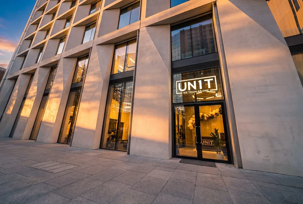 Modern building facade with large glass windows and entrance displaying illuminated UN1T sign.