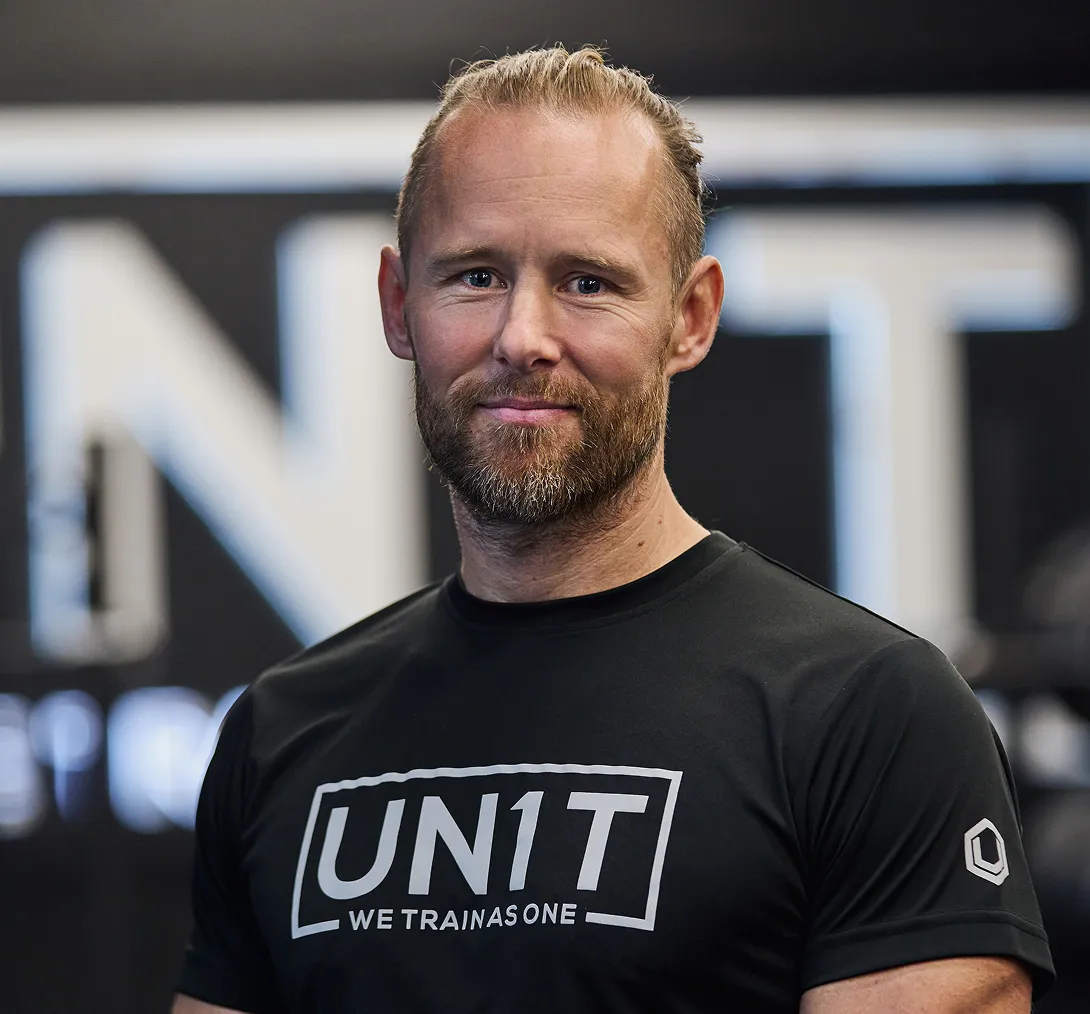 Picture of Rob wearing a black shirt with 'UN1T WE TRAIN AS ONE' text, standing indoors.