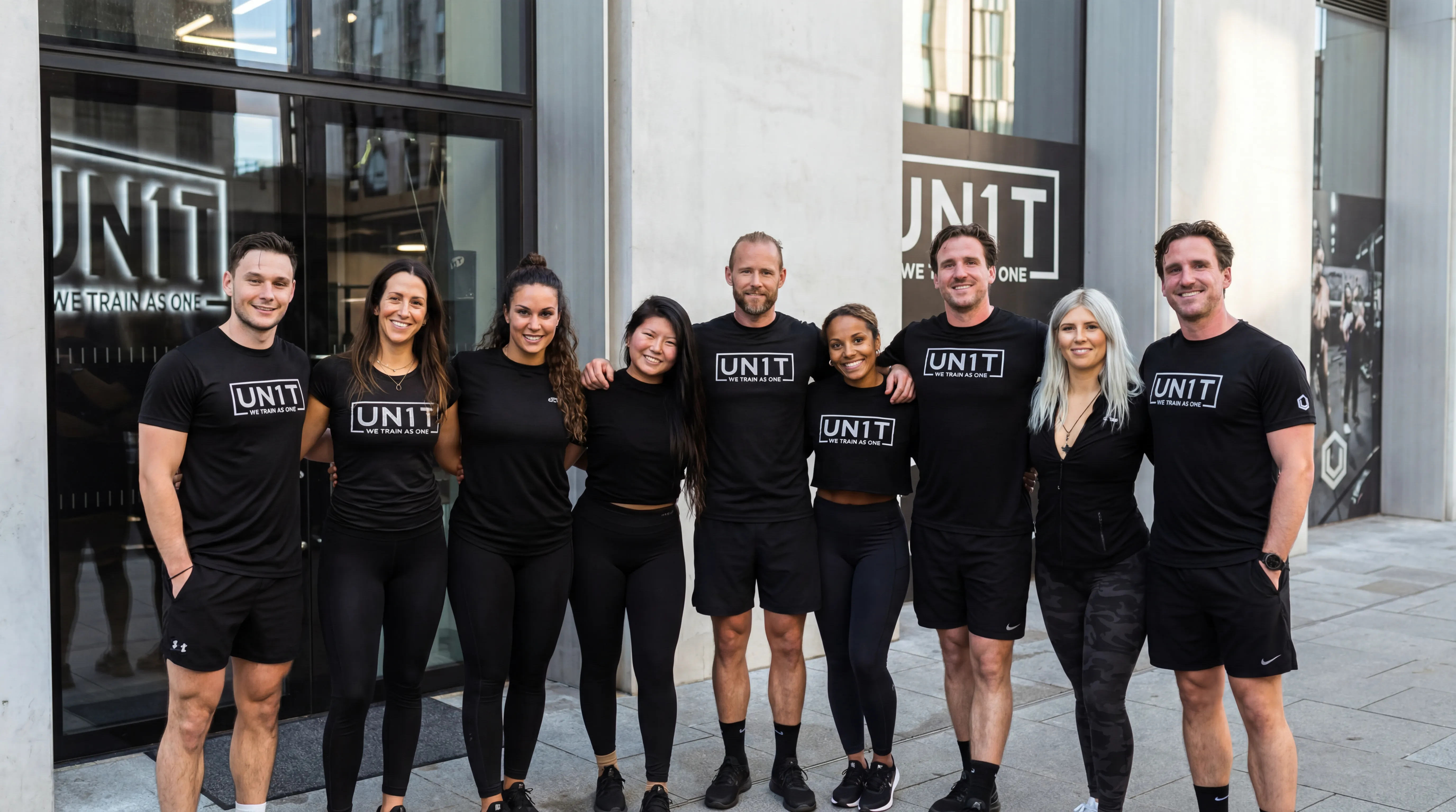 Group of nine men and women in black workout gear standing outside a building with UNIT logos.