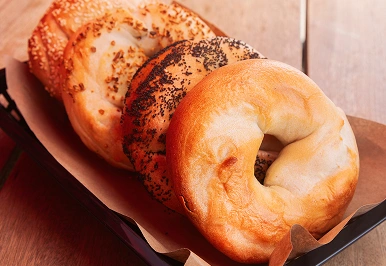 Assorted bagels sitting in a tray on a wooden table