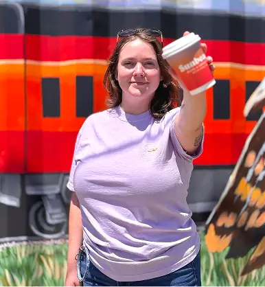 Woman smiling and holding a red sunbeam cup out towards the camera