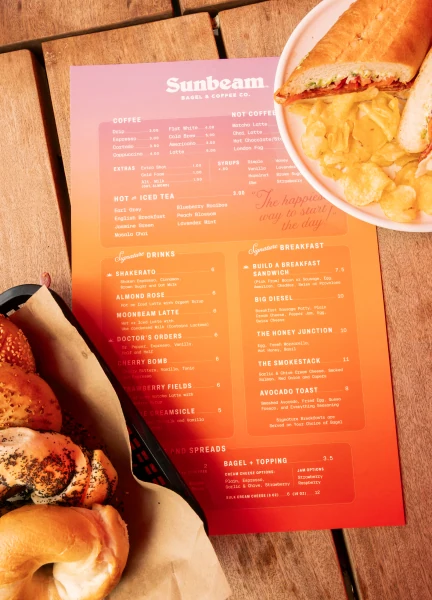 Sunbeam menu sitting on a wooden table with bagels and sandwiches sitting next to it
