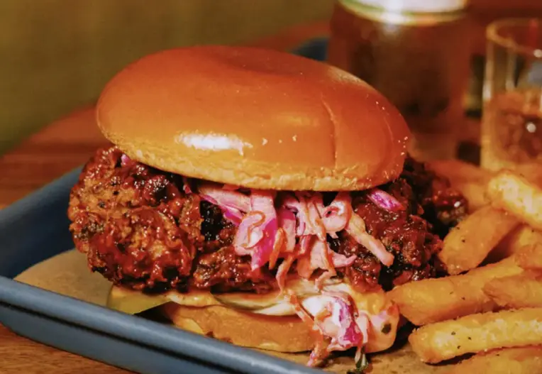 Fried chicken sandwich with coleslaw and pickles on brioche bun served with seasoned fries.
