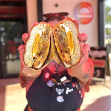 Person holding a sandwich cut in half showing melted cheese, egg, and meat inside.