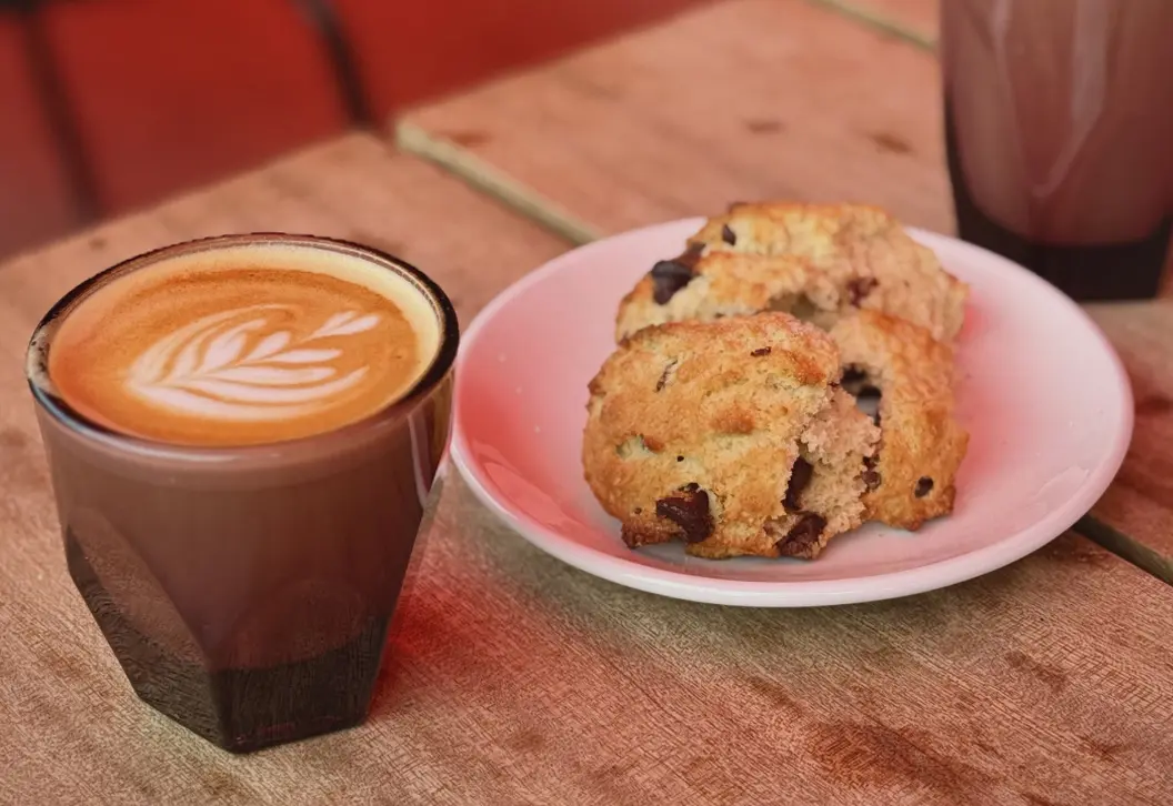 Chocolate chip scones and a coffee with foam art sitting on a table