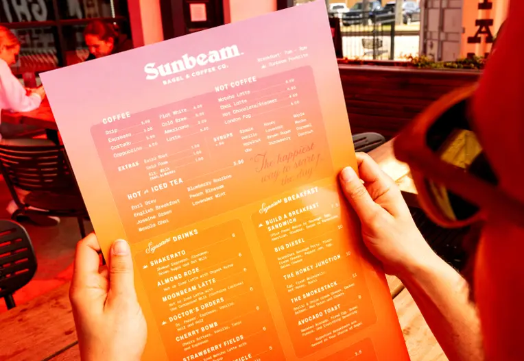 person holding the Sunbeam Bagel & Coffee Co. Menu
