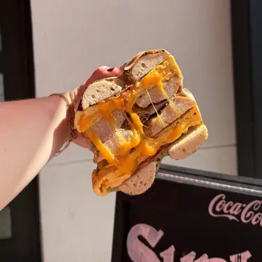 Hand holding a cheesy bagel sandwich