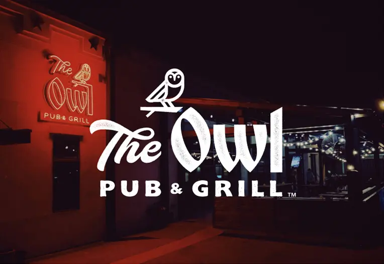 Outside of The Owl at night with The Owl Pub & Grill Logo over it