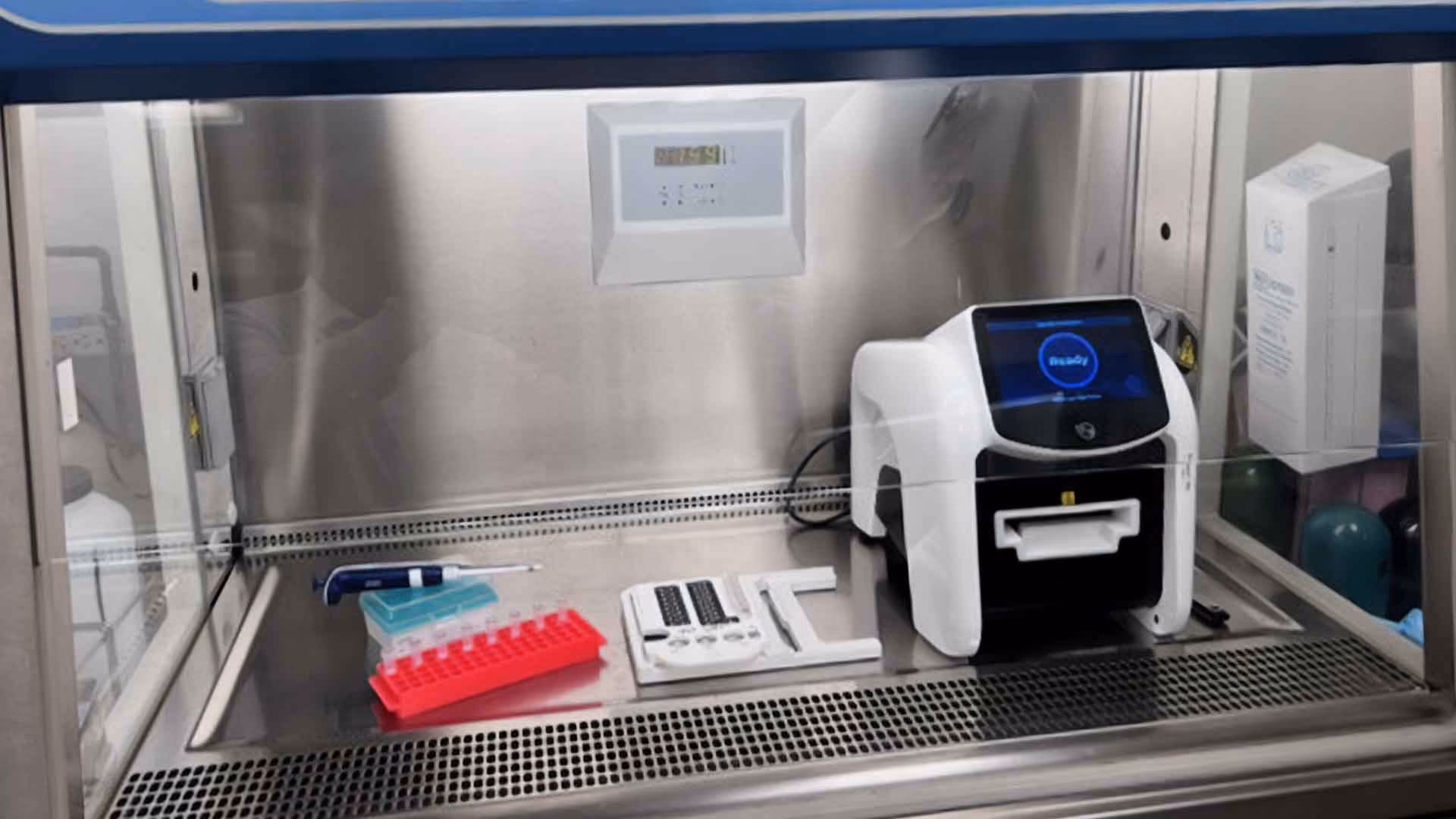 Laboratory PCR machine with pipette, tubes, and consumables on stainless steel workbench.