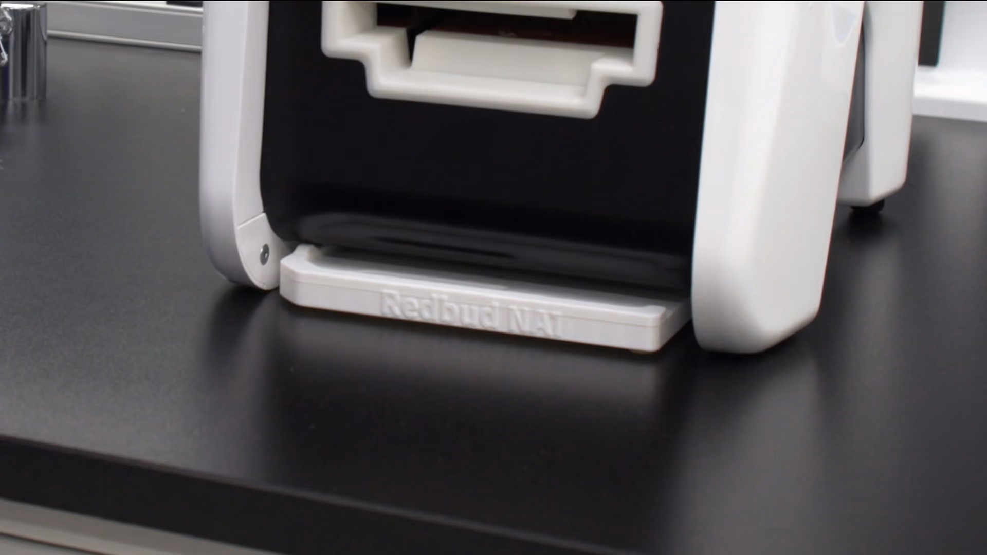 Close-up of a white and black device stand labeled Redbud NAT on a black surface.