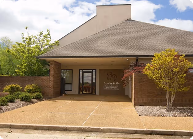 Entrance of a dental office named Tupelo Smiles with brick walls and manicured landscaping.