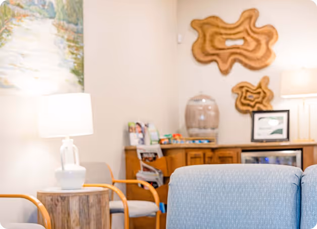 Cozy waiting room with wooden furniture, abstract wall art, and two lit table lamps.