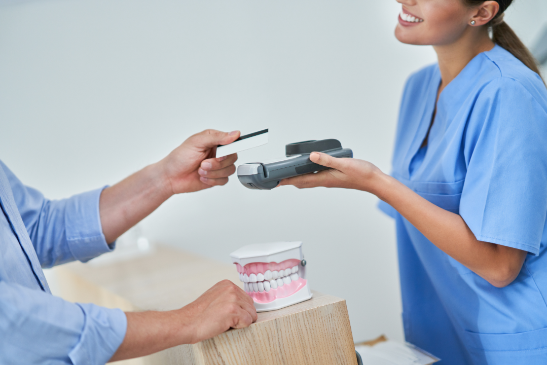 Patient paying with a card to a smiling dental hygienist holding a card reader near dental model.