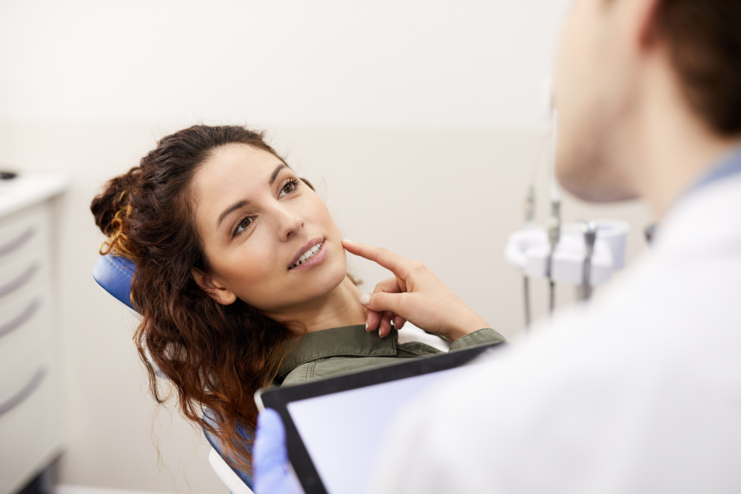Woman in dental chair talking to dentist holding a tablet during consultation.