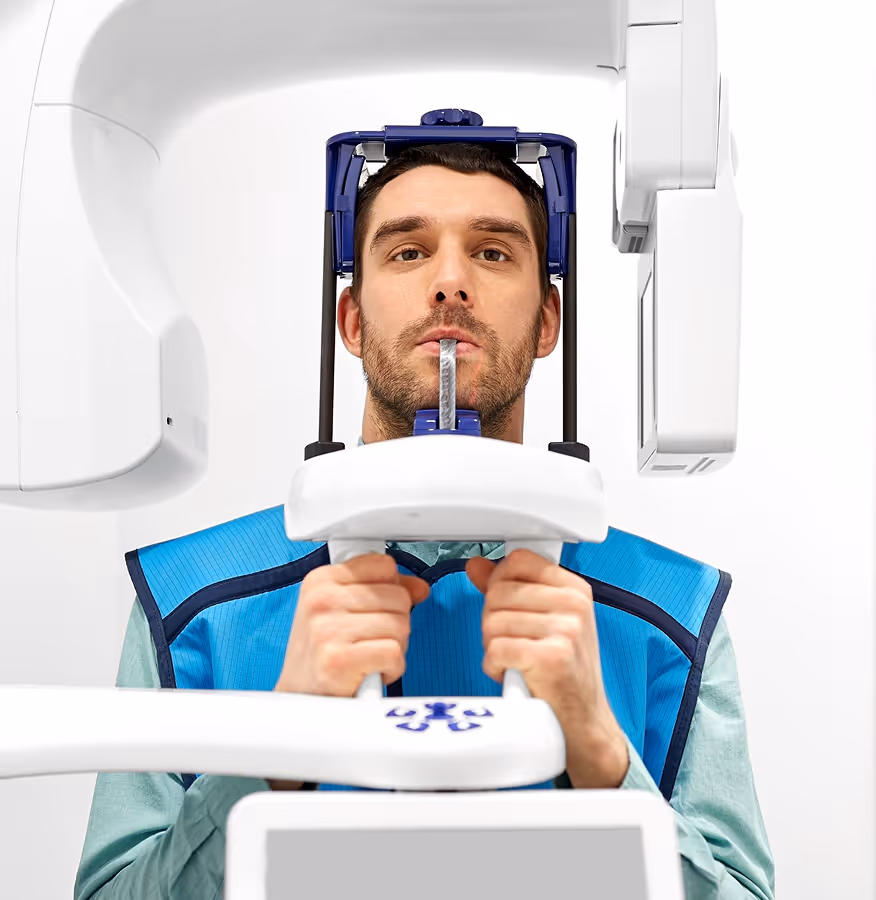 Man wearing a blue protective vest undergoing a dental or medical scan with a head-holding device.
