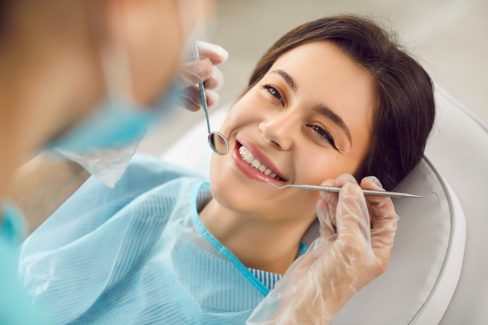 Smiling woman in dental chair being examined by dentist with dental mirror and probe.