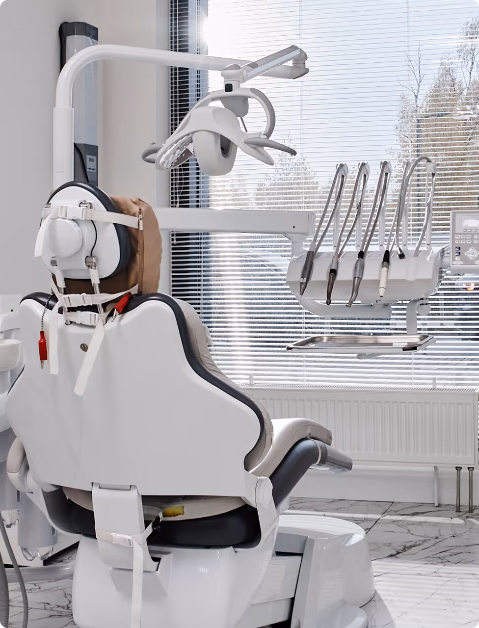 Modern dental chair with attached dental tools and overhead light in a bright clinic room.