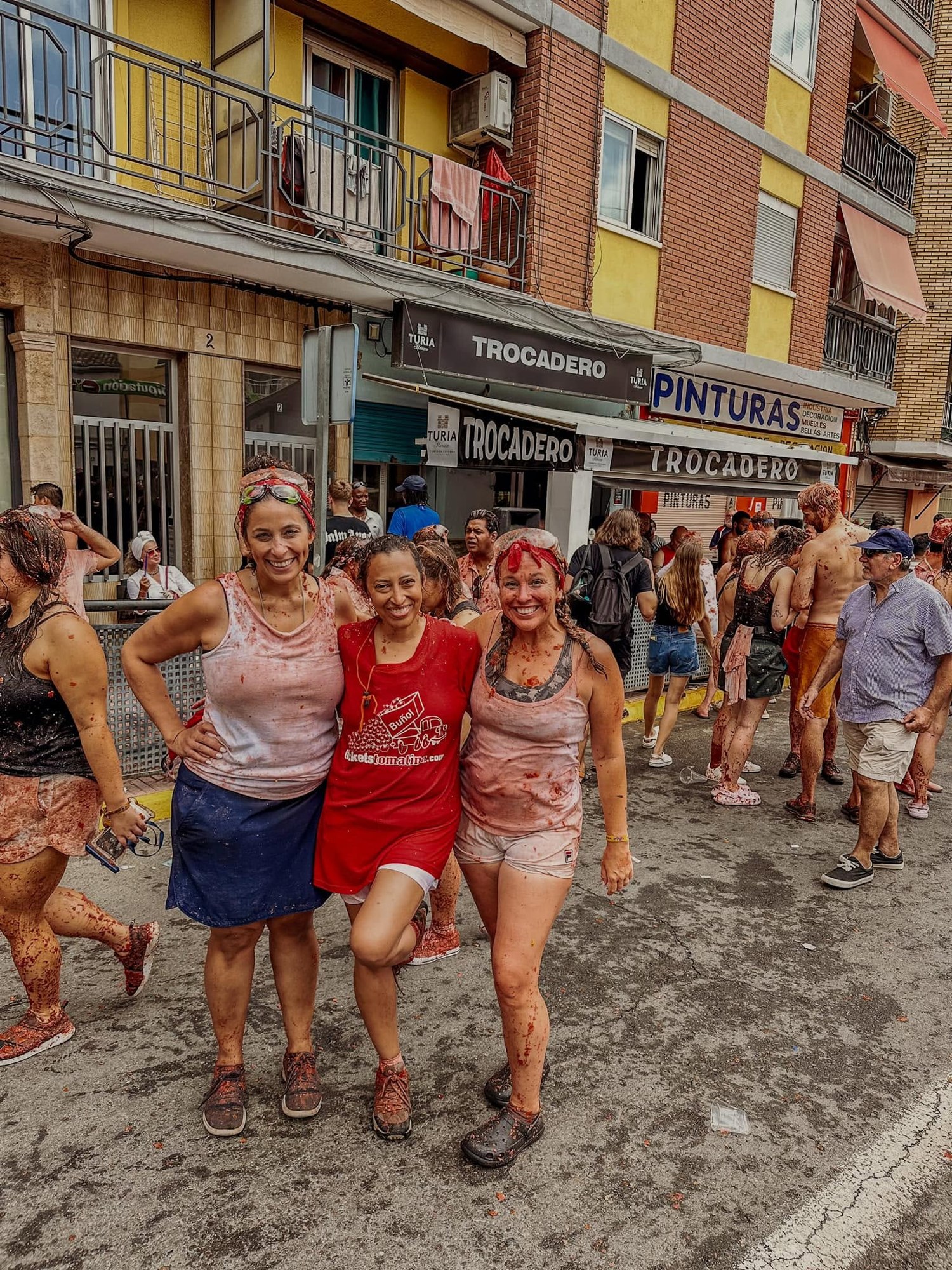 Three friends stained head to toe in tomato grin on a Buñol street after the fight.