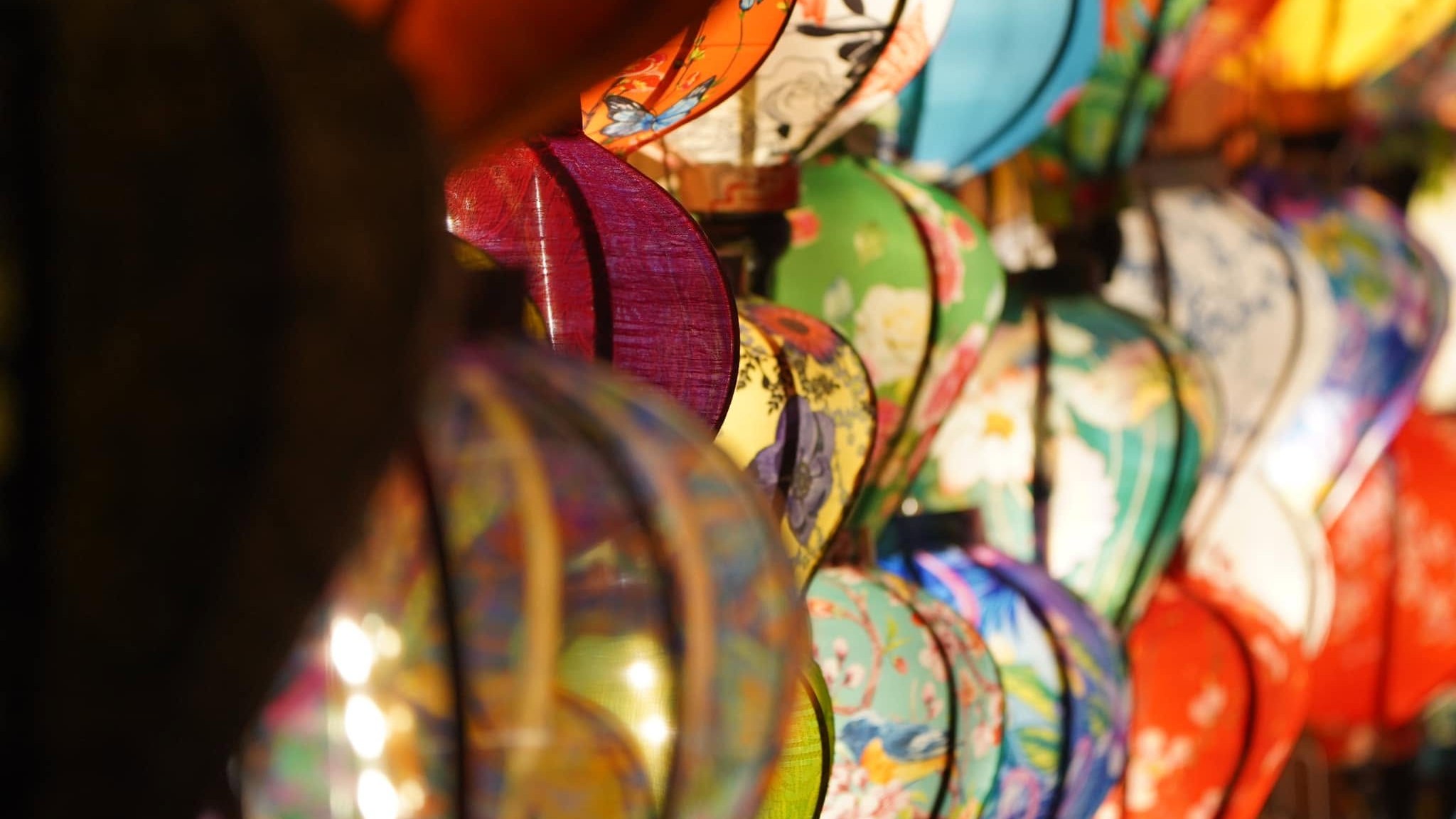 Silk lanterns painted with flowers, butterflies and birds, glowing in rows at night in Hoi An.