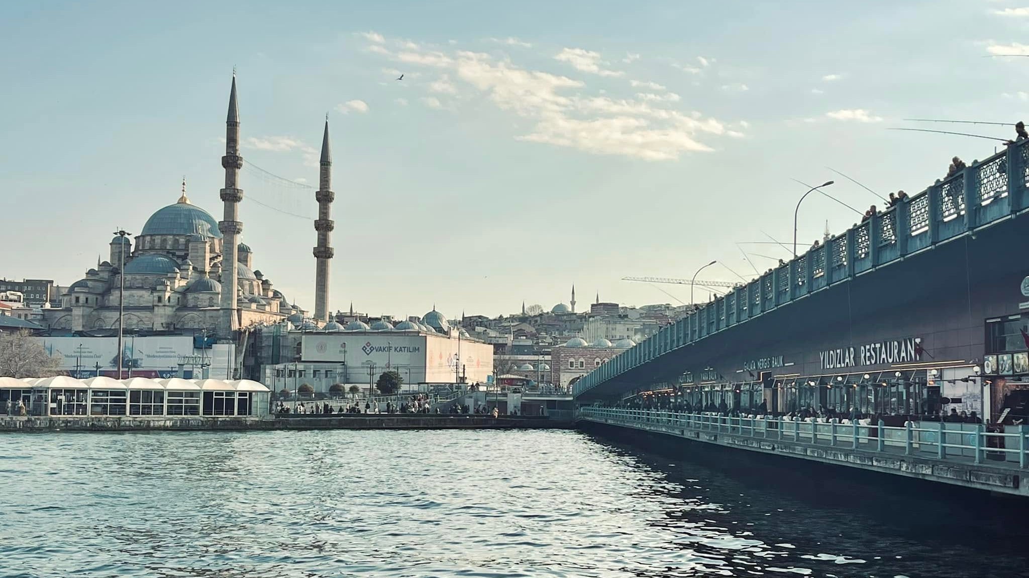 The Galata Bridge in Istanbul lined with fishermen above the restaurants on its lower level, the New Mosque across the water