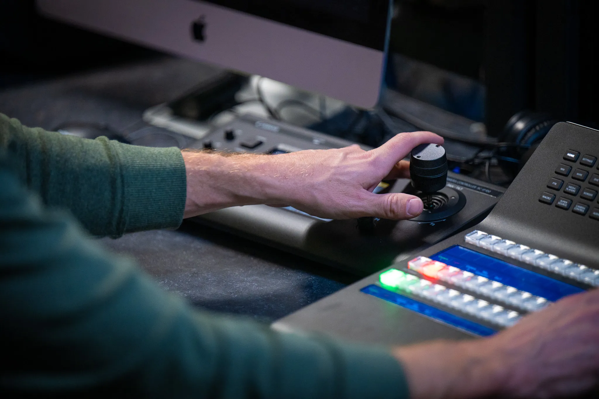 Close-up of a hand operating a PTZ camera joystick beside a Blackmagic ATEM-style switcher panel in a church control booth