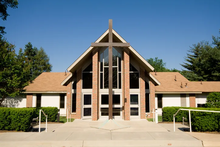 Exterior of a brick church building with a large wooden cross at the peak of a glass-front sanctuary entrance.