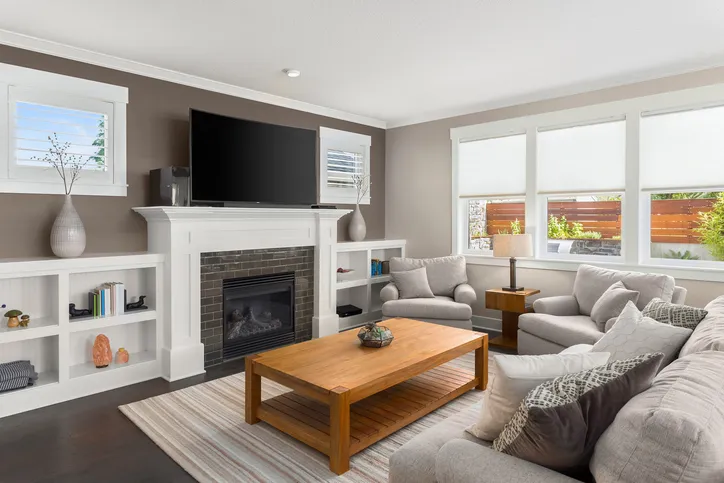 Living room with a wall-mounted TV above a white fireplace mantel, gray sofa and armchairs, and a wood coffee table.