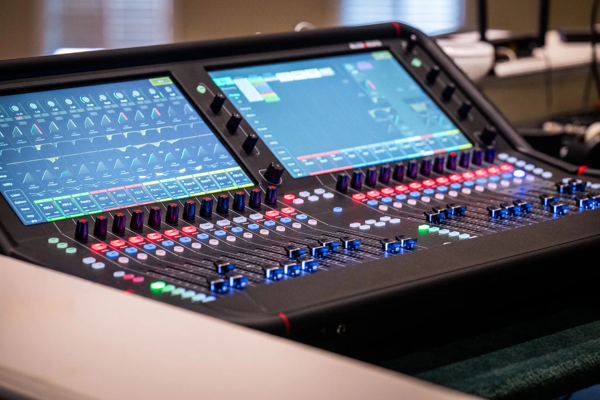 Close-up of an Allen & Heath Avantis digital mixer's touchscreens showing EQ curves and input channels, with illuminated faders in the foreground.