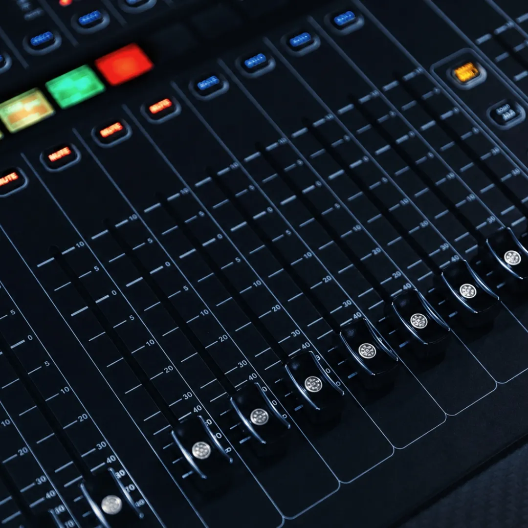 Angled close-up of a digital mixer's fader bank with staggered fader levels and illuminated mute buttons