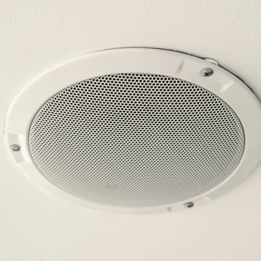 Close-up of a white in-ceiling speaker grille flush-mounted in a textured ceiling