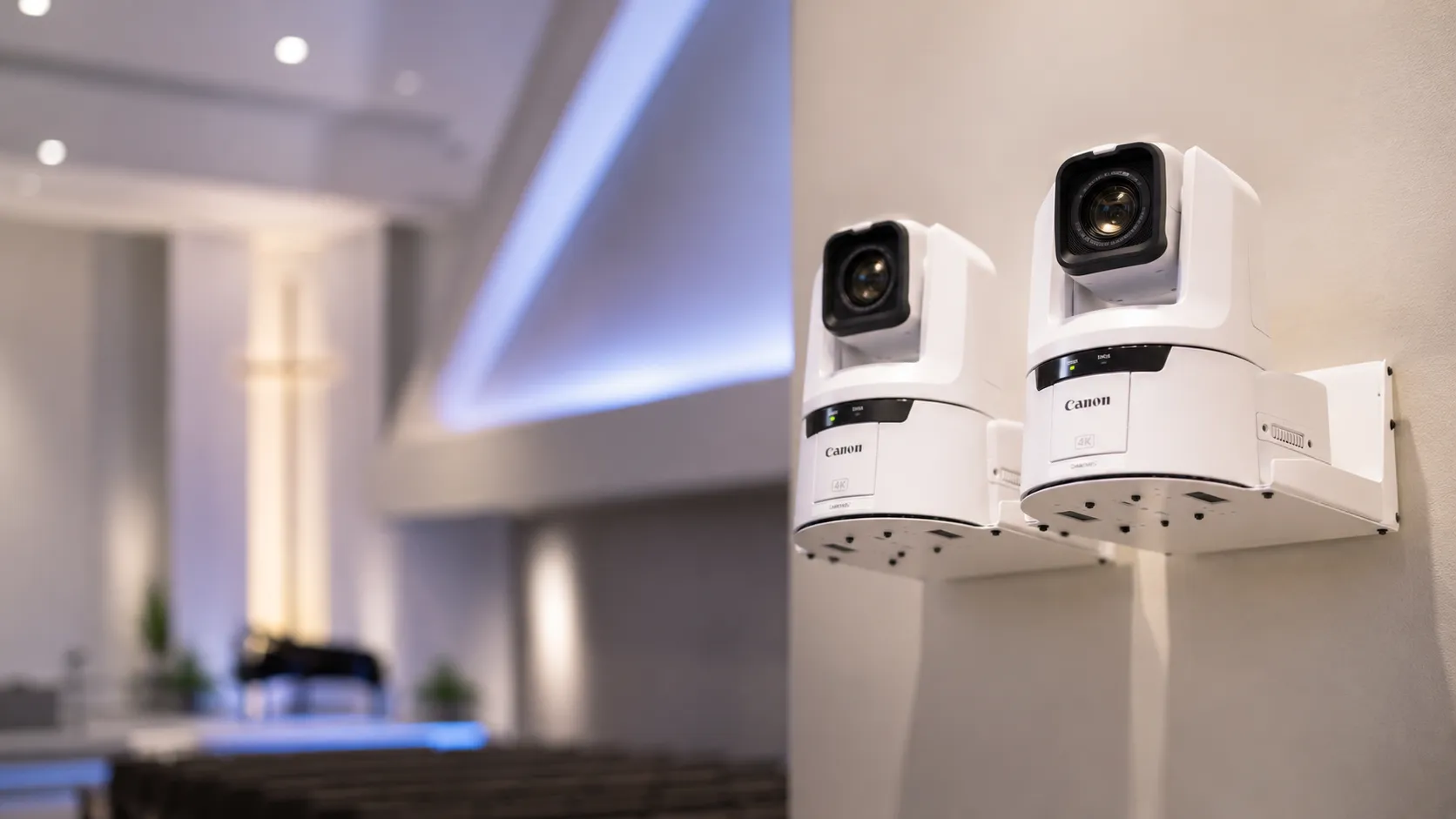 Two wall-mounted Canon 4K PTZ cameras in the foreground, with an illuminated stage cross and grand piano visible on the blurred sanctuary platform behind