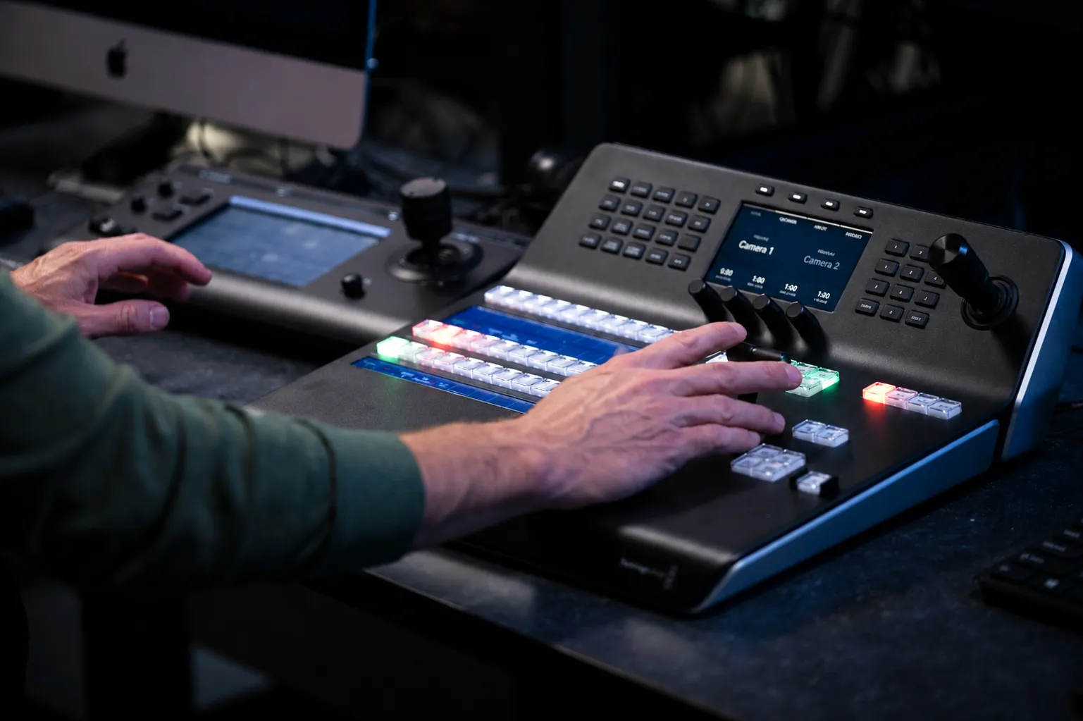 Close-up of a hand operating a PTZ camera joystick beside a Blackmagic ATEM-style switcher panel in a church control booth