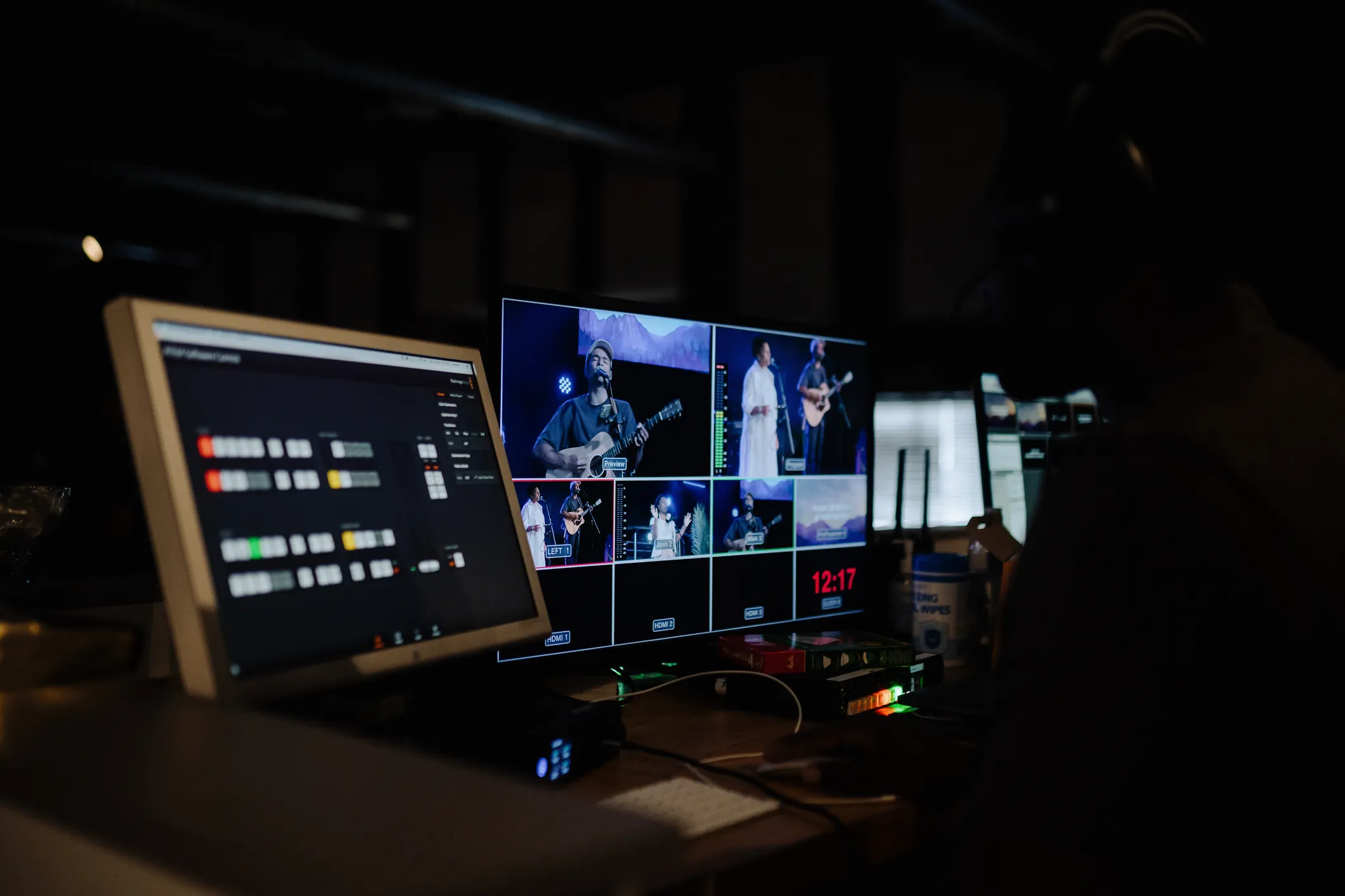 Two monitors in a dim production booth showing a multiview of a live worship band feed, with preview, program, and camera-label overlays