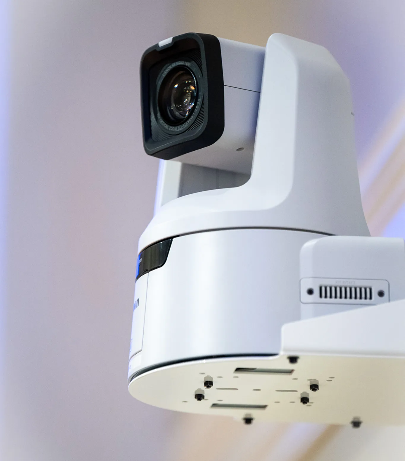 Macro close-up of a ceiling-mounted Canon 4K PTZ camera, showing the lens and mounting bracket against a softly lit background