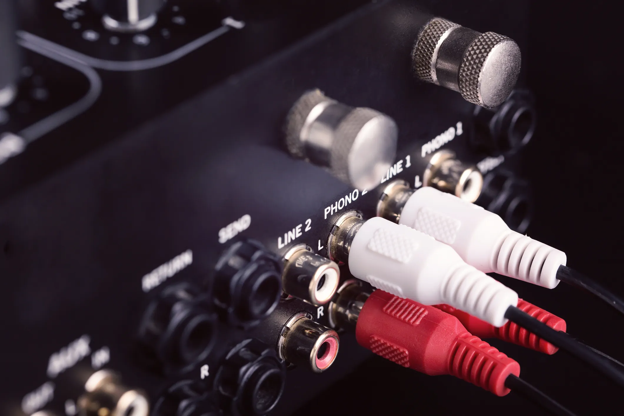 Close-up of RCA phono and line input jacks on a DJ mixer, with red and white cables connected