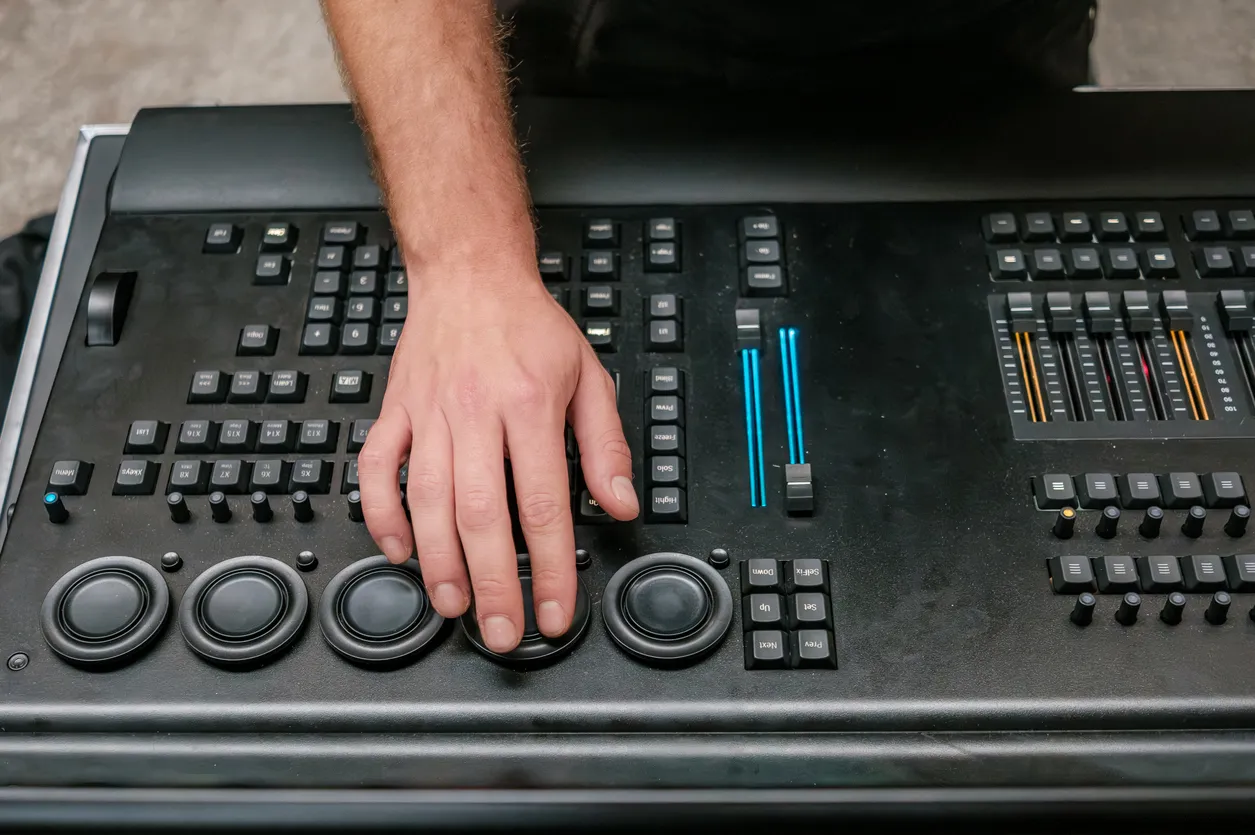 Hand operating encoder wheels on a lighting control console, with blue motorized faders and a fader bank visible