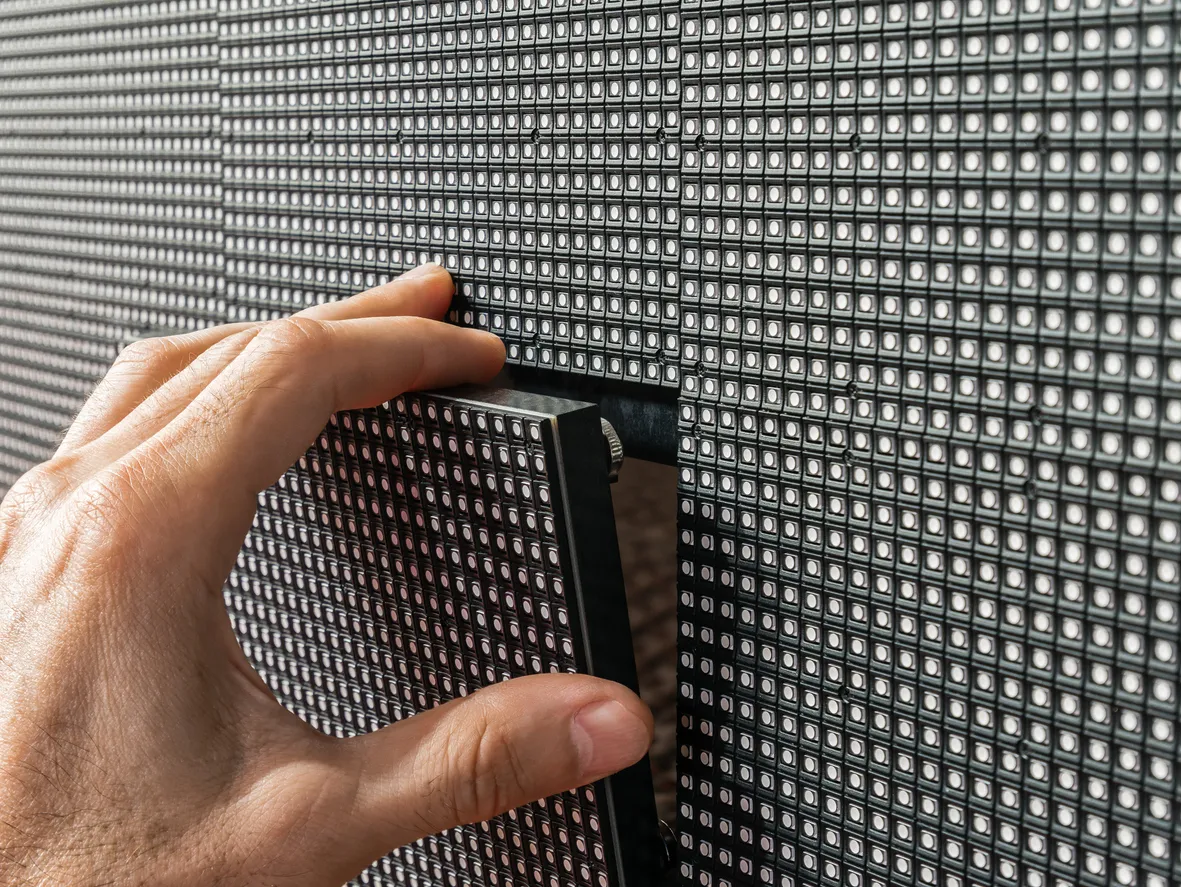 Hand fitting an individual LED panel into a modular video wall, showing the tight pixel grid up close