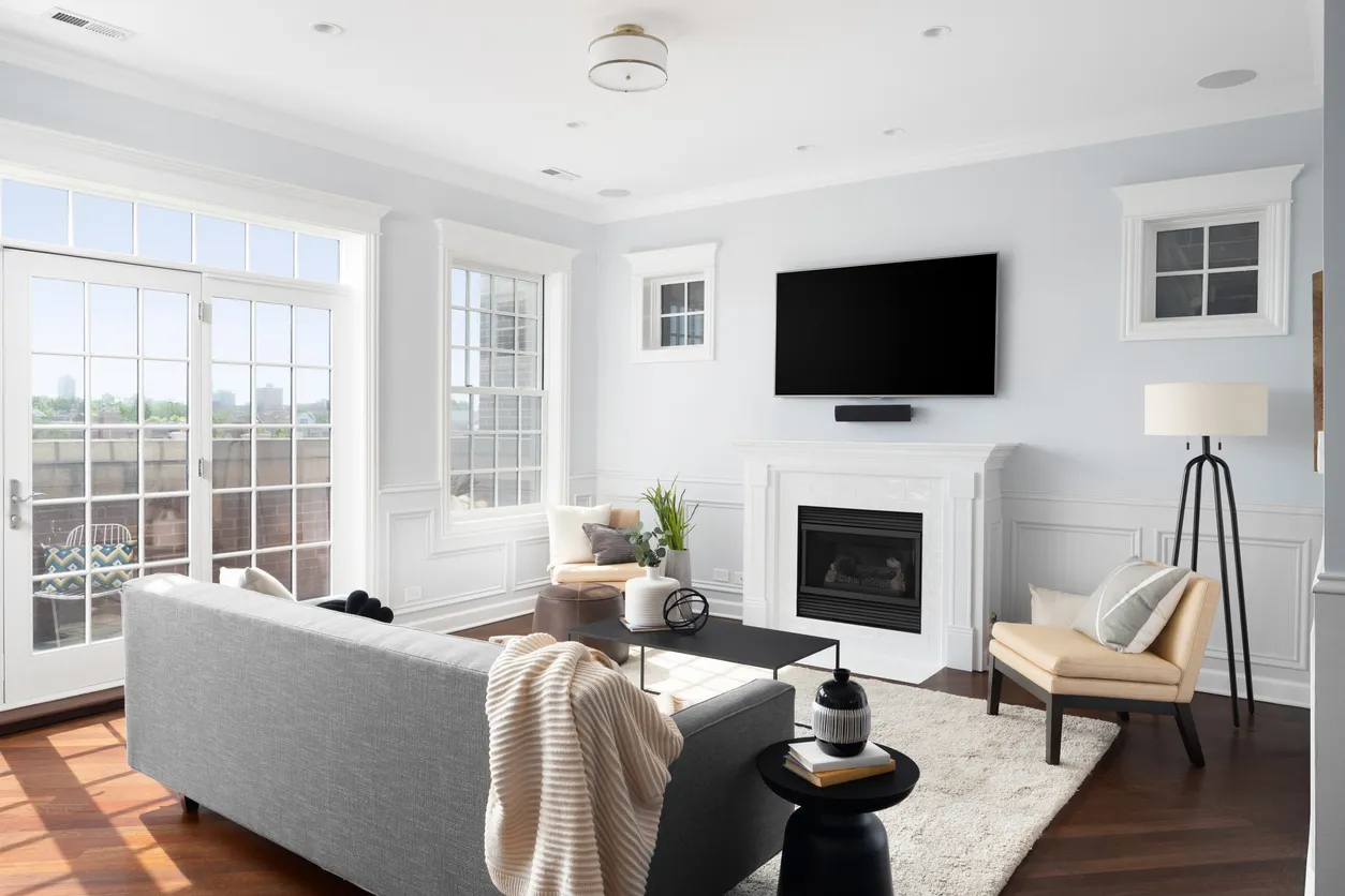 Living room with a wall-mounted TV above a white fireplace, gray sofa, and French doors opening onto a rooftop terrace