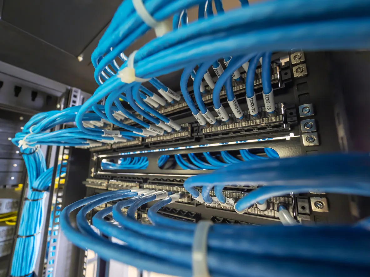 Wide-angle close-up of a server rack's blue Cat cables looped and routed into a patch panel with COM3 port labels
