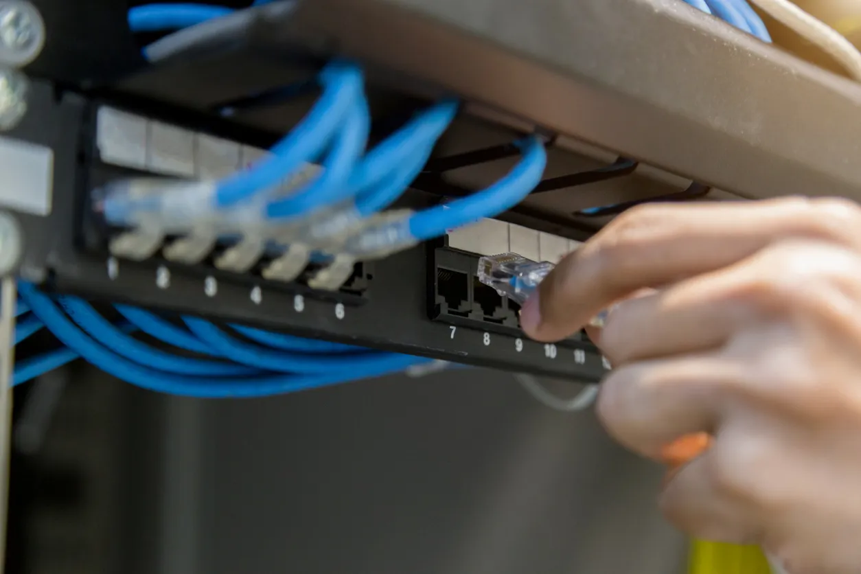 Close-up of a hand plugging an RJ45 cable into a numbered patch panel port, surrounded by blue Cat cables