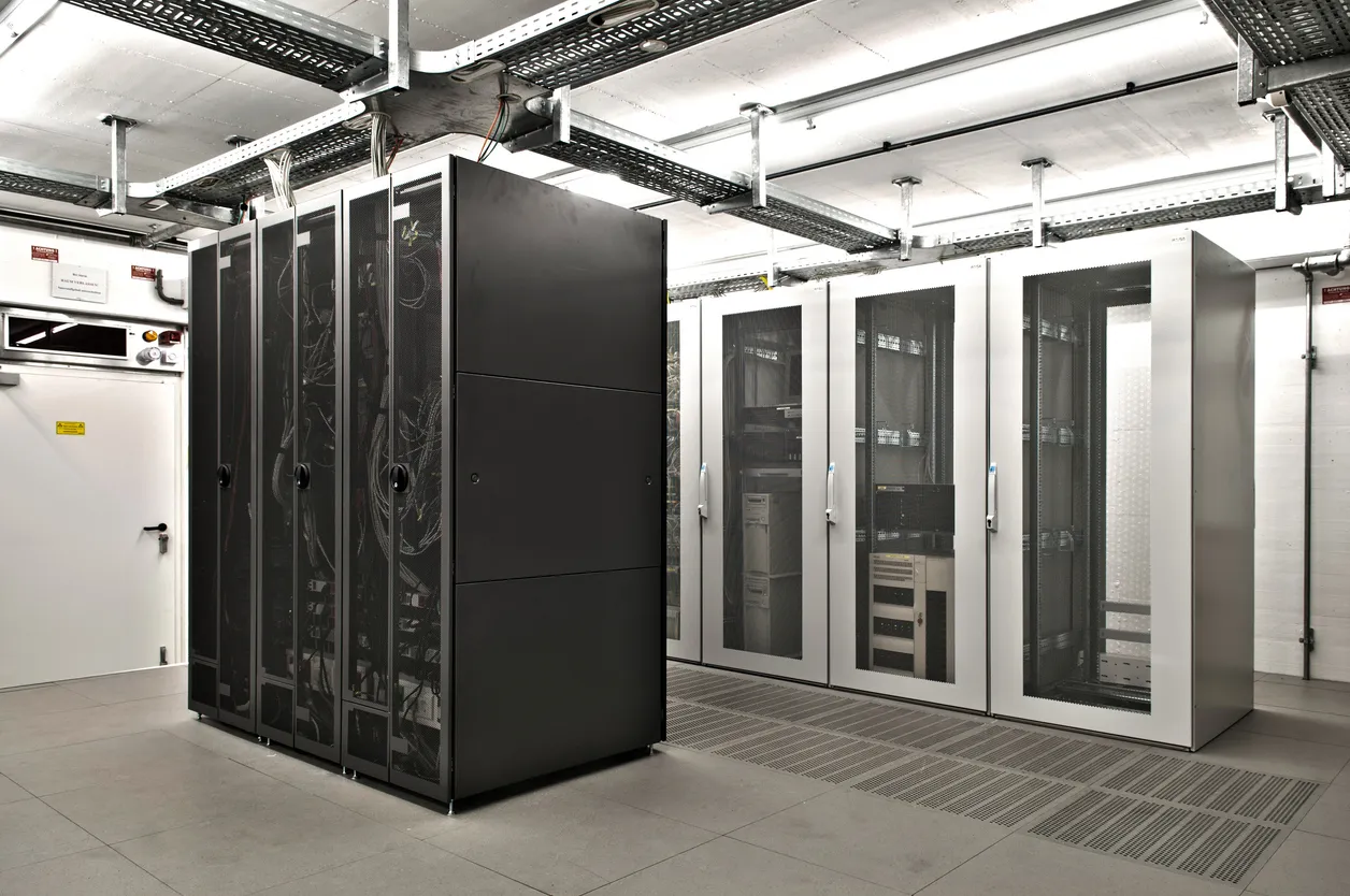 Row of black and white server racks in a data center with overhead cable trays and raised access flooring