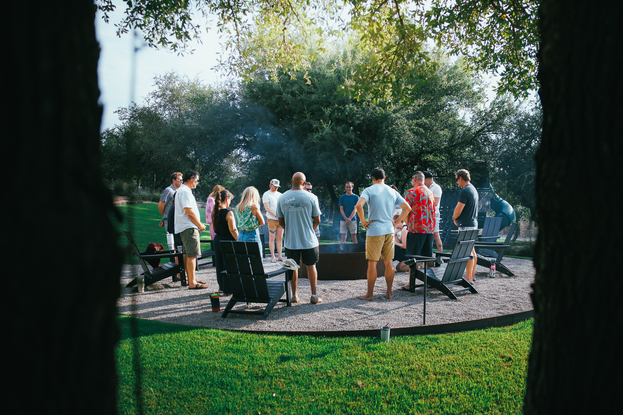 A group standing in a circle around a fire pit on the lawn
