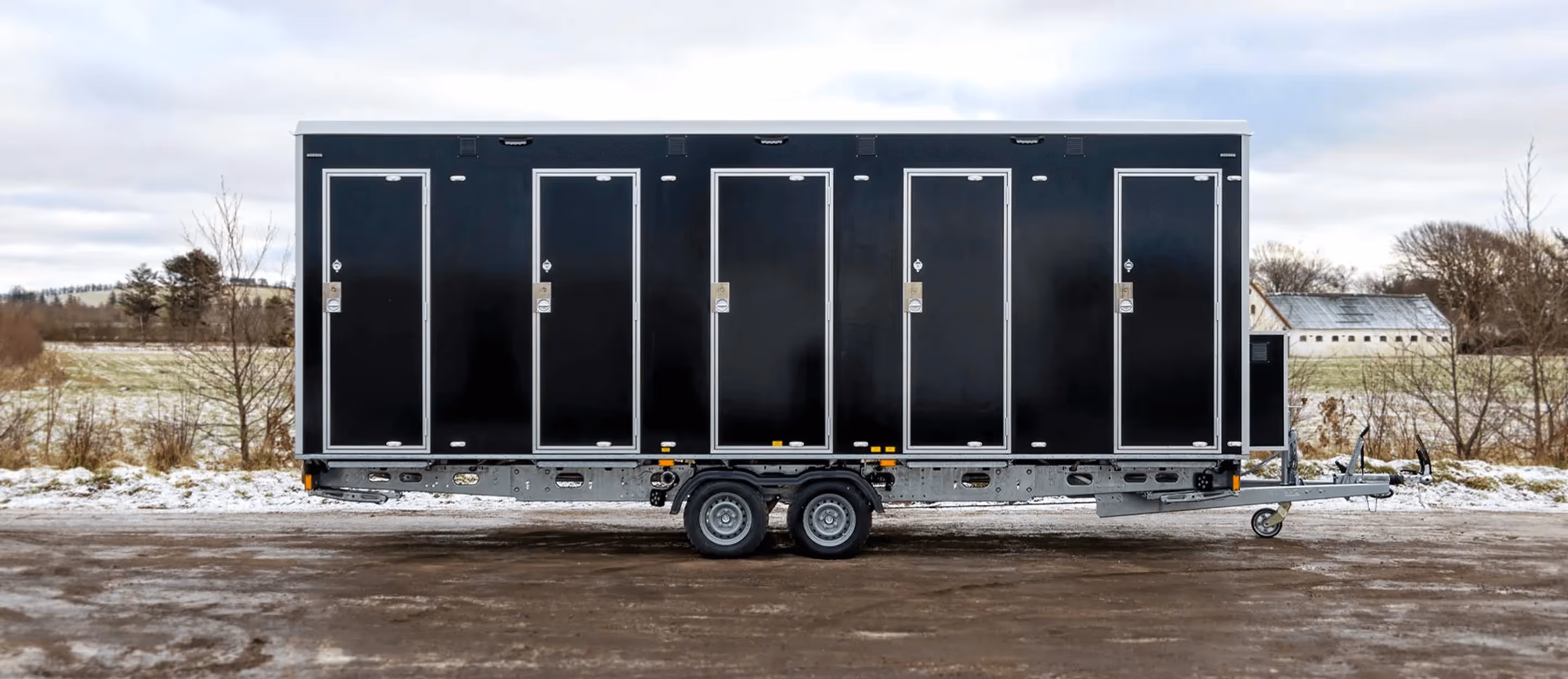 Black shower trailer with five side doors and dual axle wheels parked outdoors in a rural area