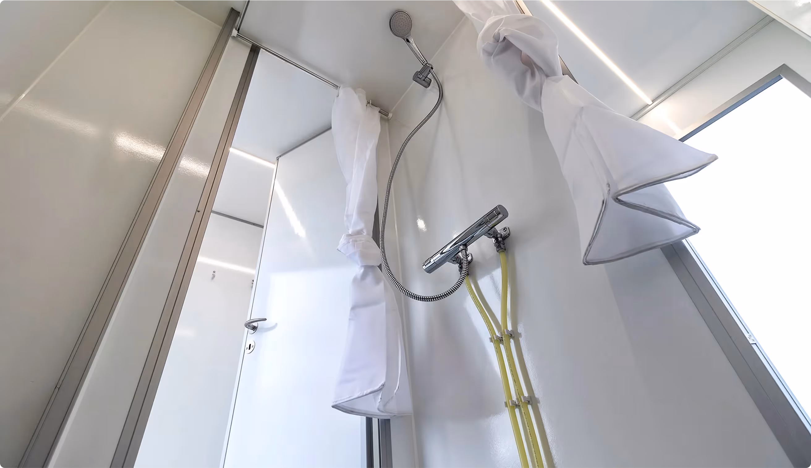 Shower interior with closed white curtain, hand-held showerhead, and visible temperature control with yellow hoses